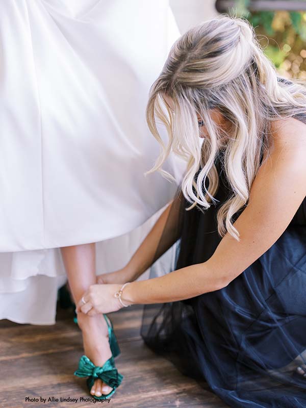 Bridesmaid helps bride put on green wedding shoes