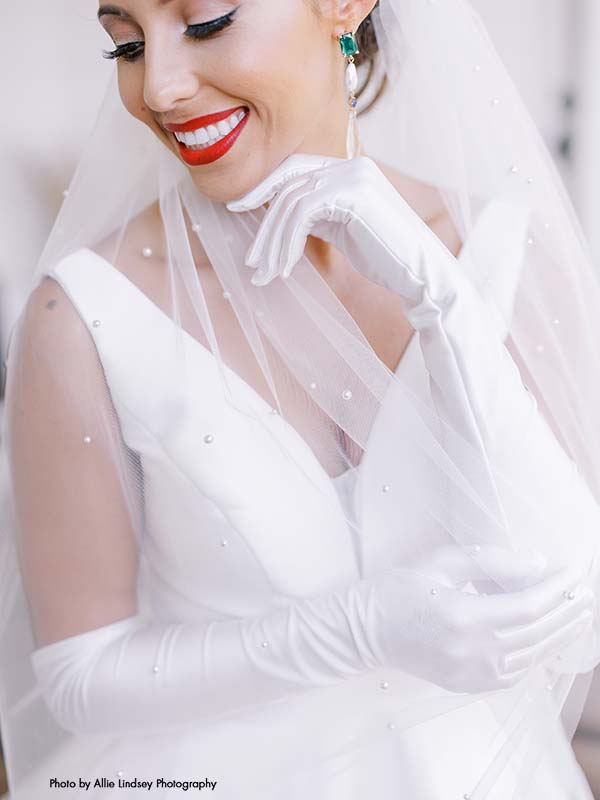 Bride with red lipstick wearing a pearl veil and elbow-length gloves