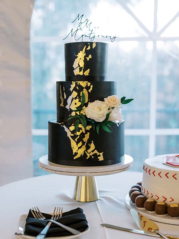 3-tier black wedding cake with gold foil and fresh white flowers