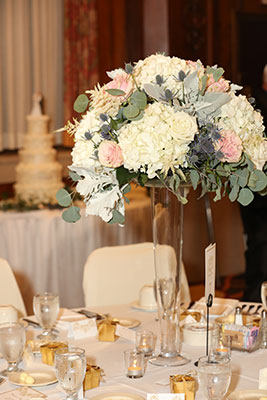 Tall centerpiece with greenery, white roses, and blue thistle by Renning's FLowers