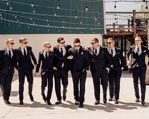 Groomsmen and groom walk outside in custom black suits by Daniel's Custom Clothing