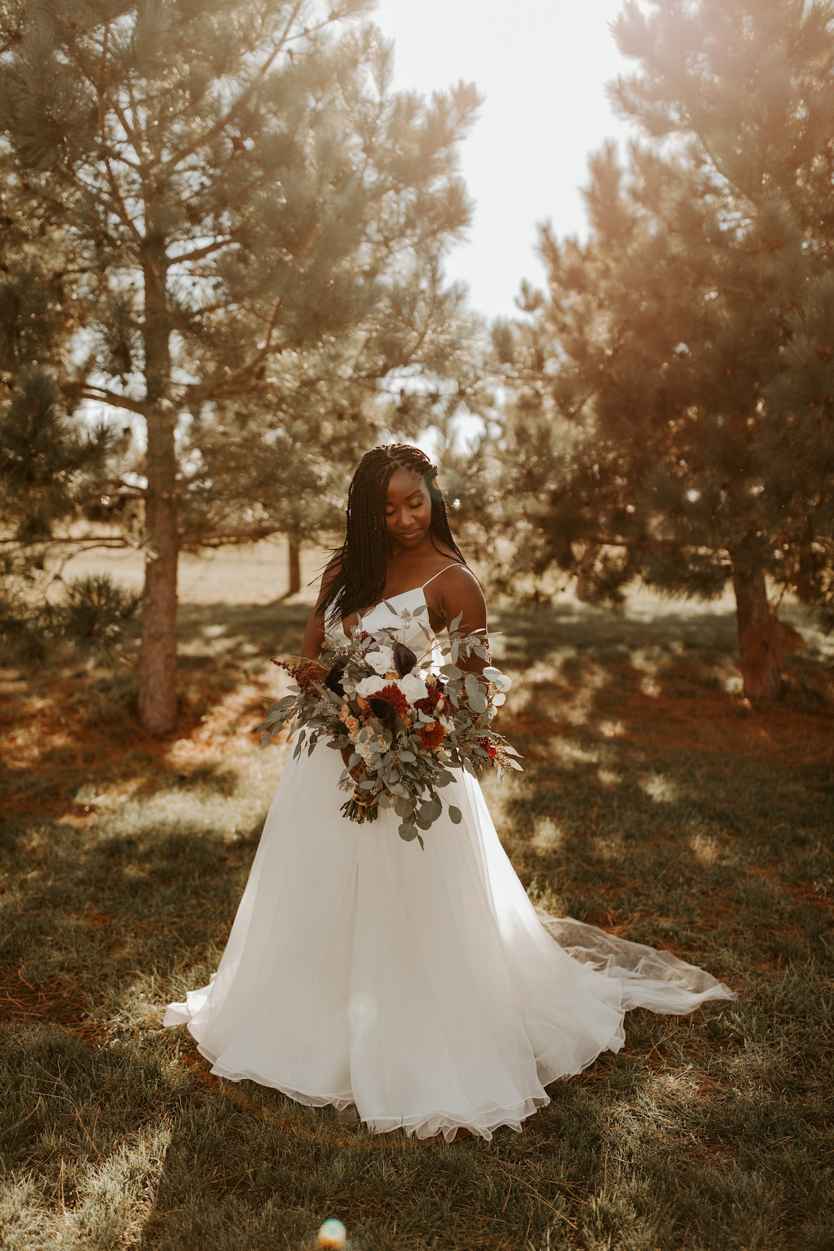 Bride in a-line gown stands in front of fall trees