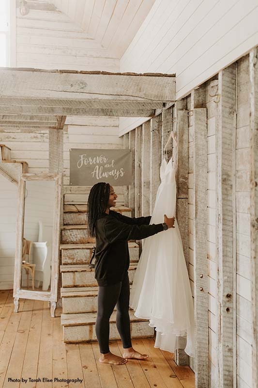 Bride holds bridal gown hanging on rustic walls