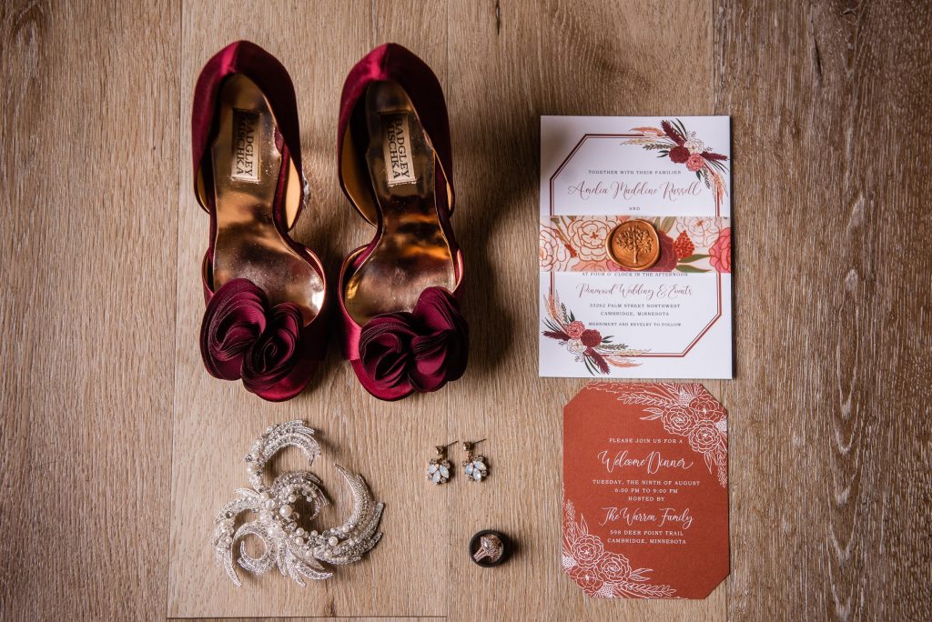 Red bridal shoes sit next to orange boho wedding invitation