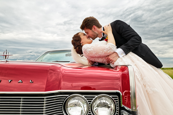 Couple kisses on hood of classic car