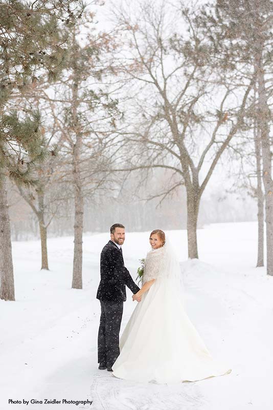 Bride and groom walk through woods at winter wedding