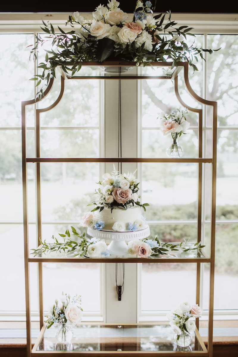 2-tier white wedding cake with flowers sits on shelf