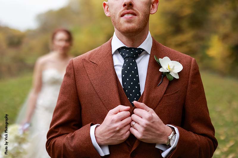 Groom in brown suit and polka dot tie with orchid boutonniere