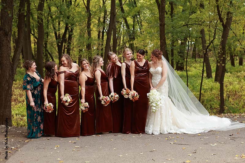 Bridesmaids in burgundy dresses stand outside with bride