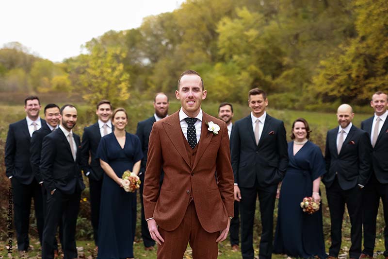 Groom in brown suit and wedding party with navy suits and dresses