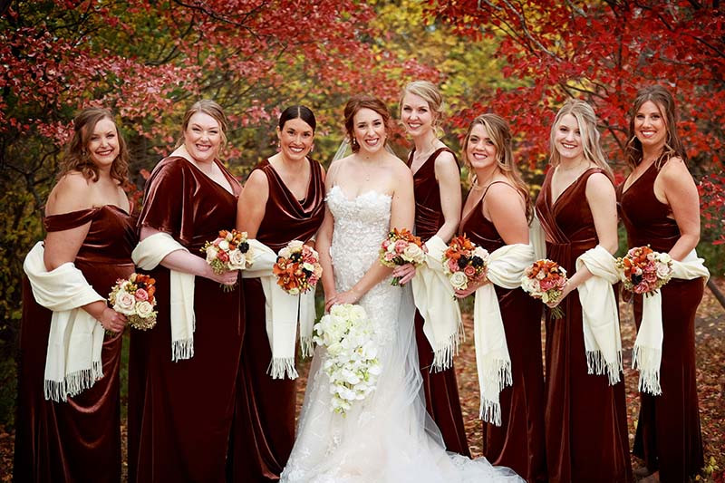 Wedding party in burgundy dresses and cream shawls post with bride