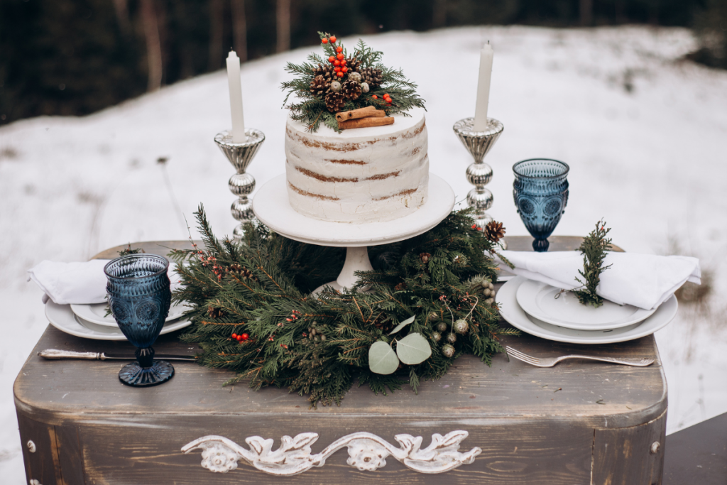 Single-tier naked white cake sits on pine wreath at winter wedding
